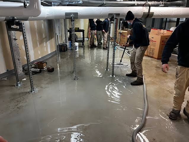 Restoration technicians extracting hidden moisture and standing floodwater from concrete slab